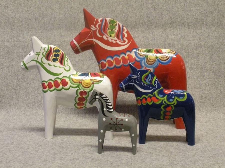 Tre dalahästar, en vit en röd, en blå i olika storlekar, en grå Faluhäst med svart och vitt mönster.