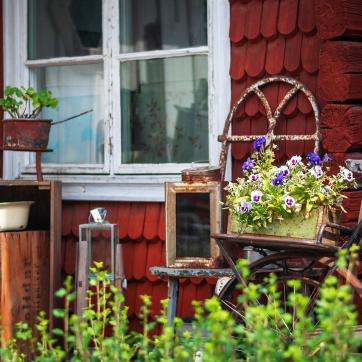Äldre föremål och blommor framför en röd husvägg.
