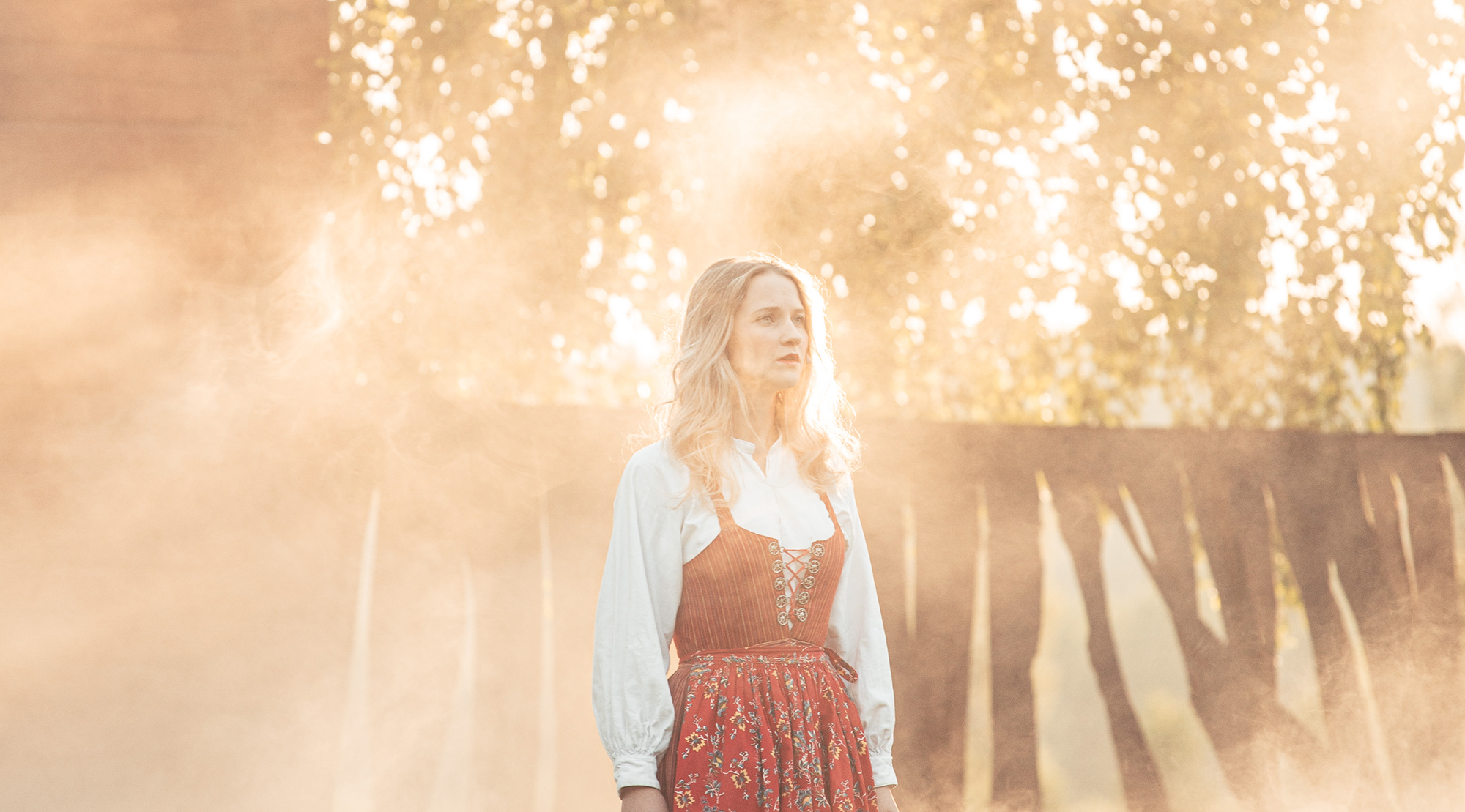 En blond kvinna i folkdräkt står på en scen i motljus.