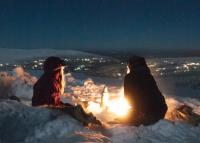 Två personer kring öppen eld i vinternatten.