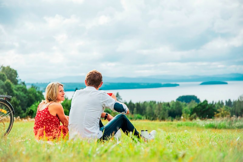 Ett par som sitter på en äng och blickar ut över sjön Siljan.