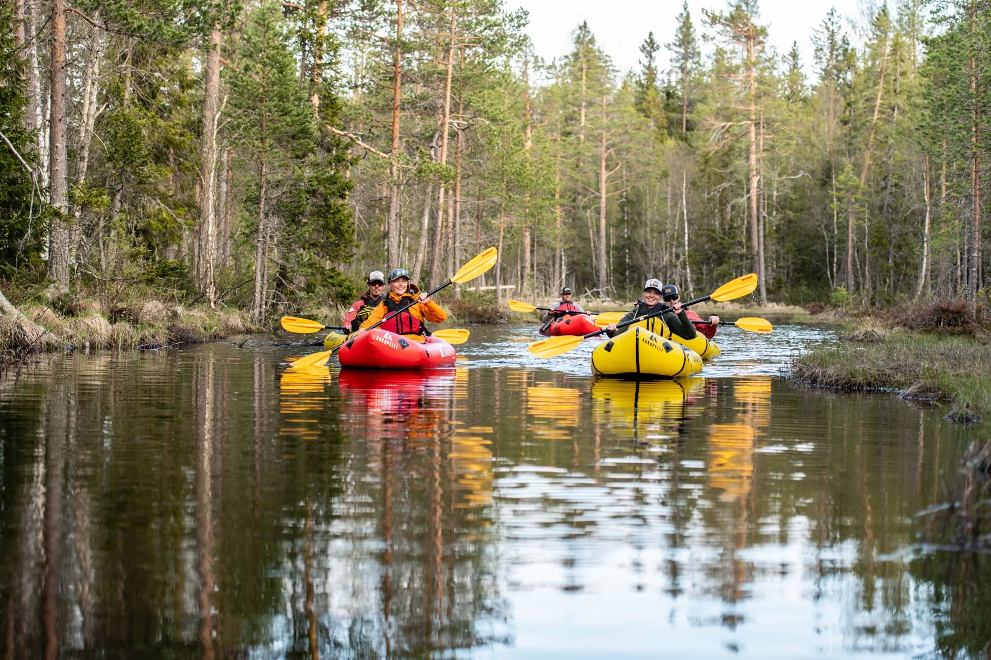 En grupp paddlar packraft i ett vattendrag i skogen.