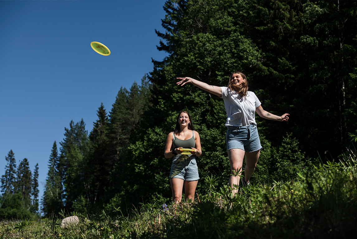 Två kvinnor spelar discgolf och kastar en frisbee.
