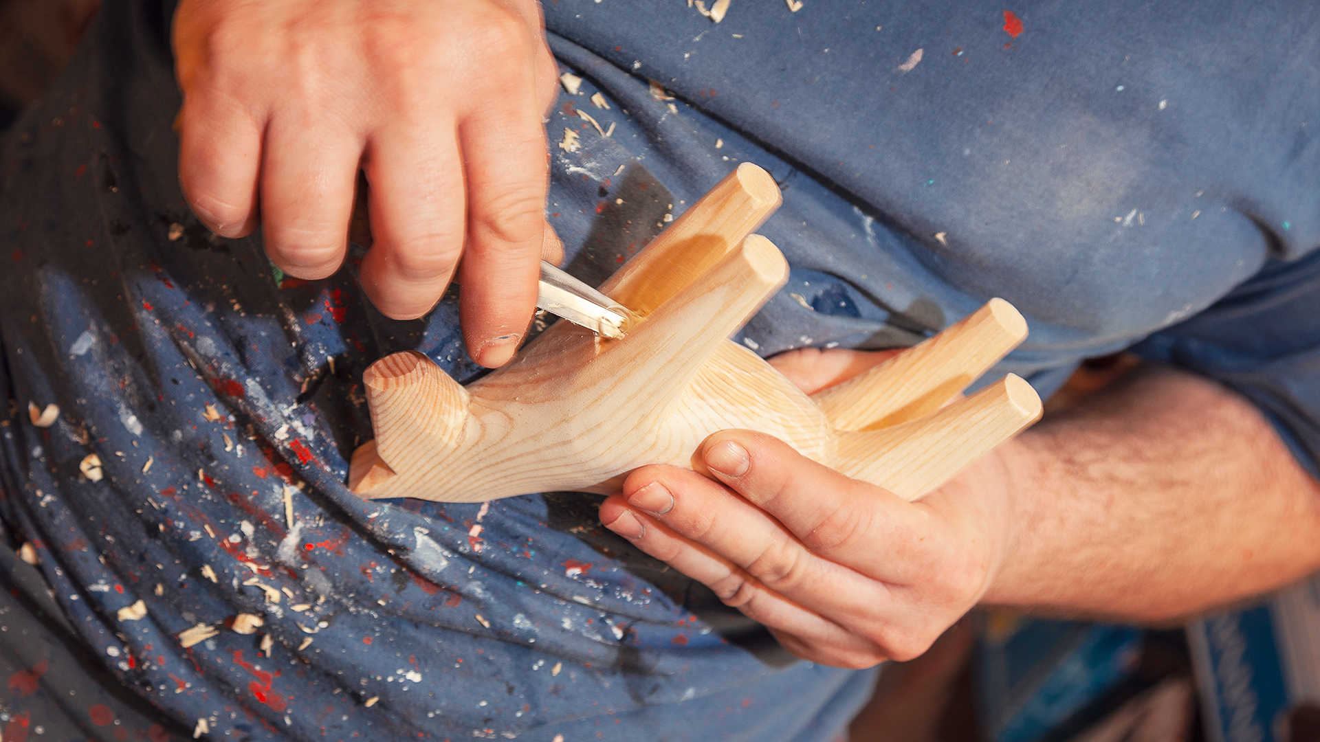 Två händer håller i och täljer en trären dalahäst.