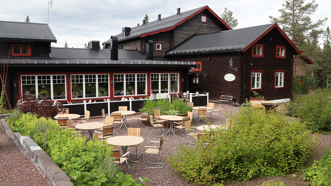 Ett mörkt timrat hotell med röda fönster och utemöbler framför i grupp.