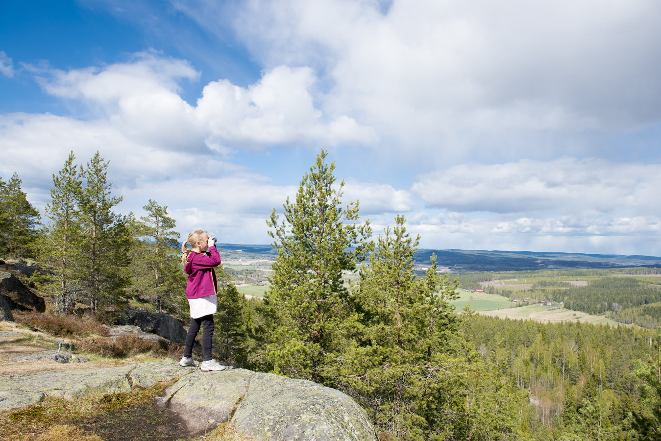Tjej som står på en klippa med kikare.