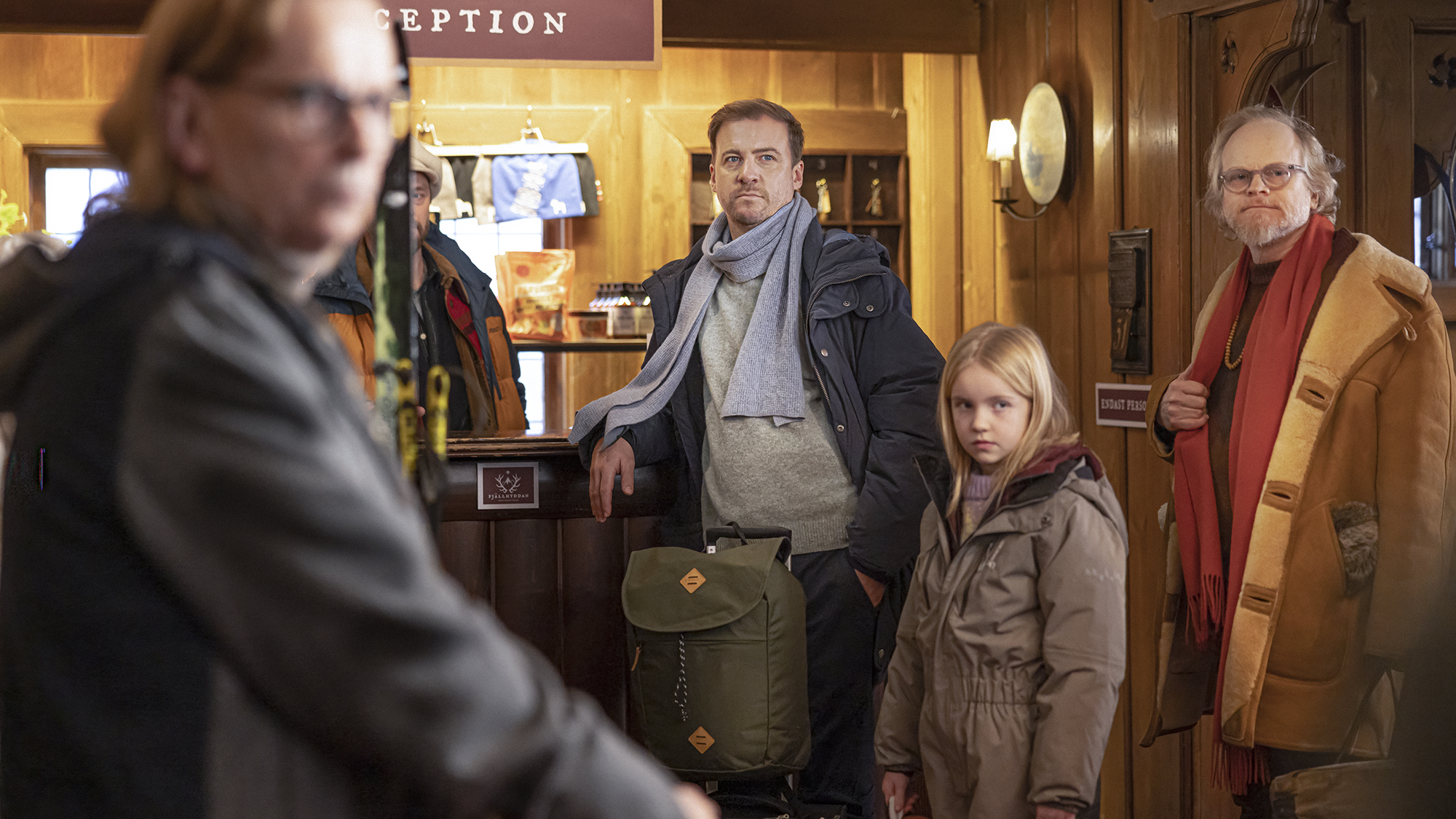 Två män och en flicka i vinterkläder står i receptionen till ett fjällhotell.