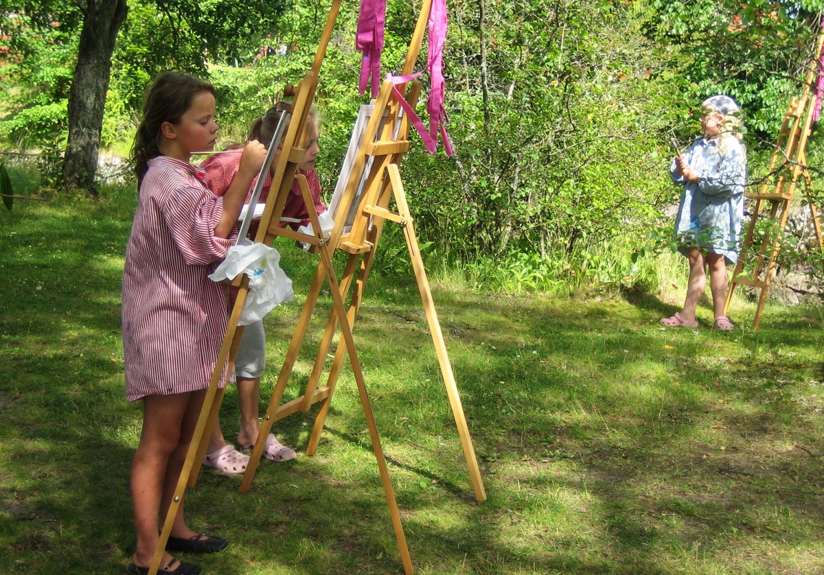Tre barn målar på stafflier utomhus i en trädgård.