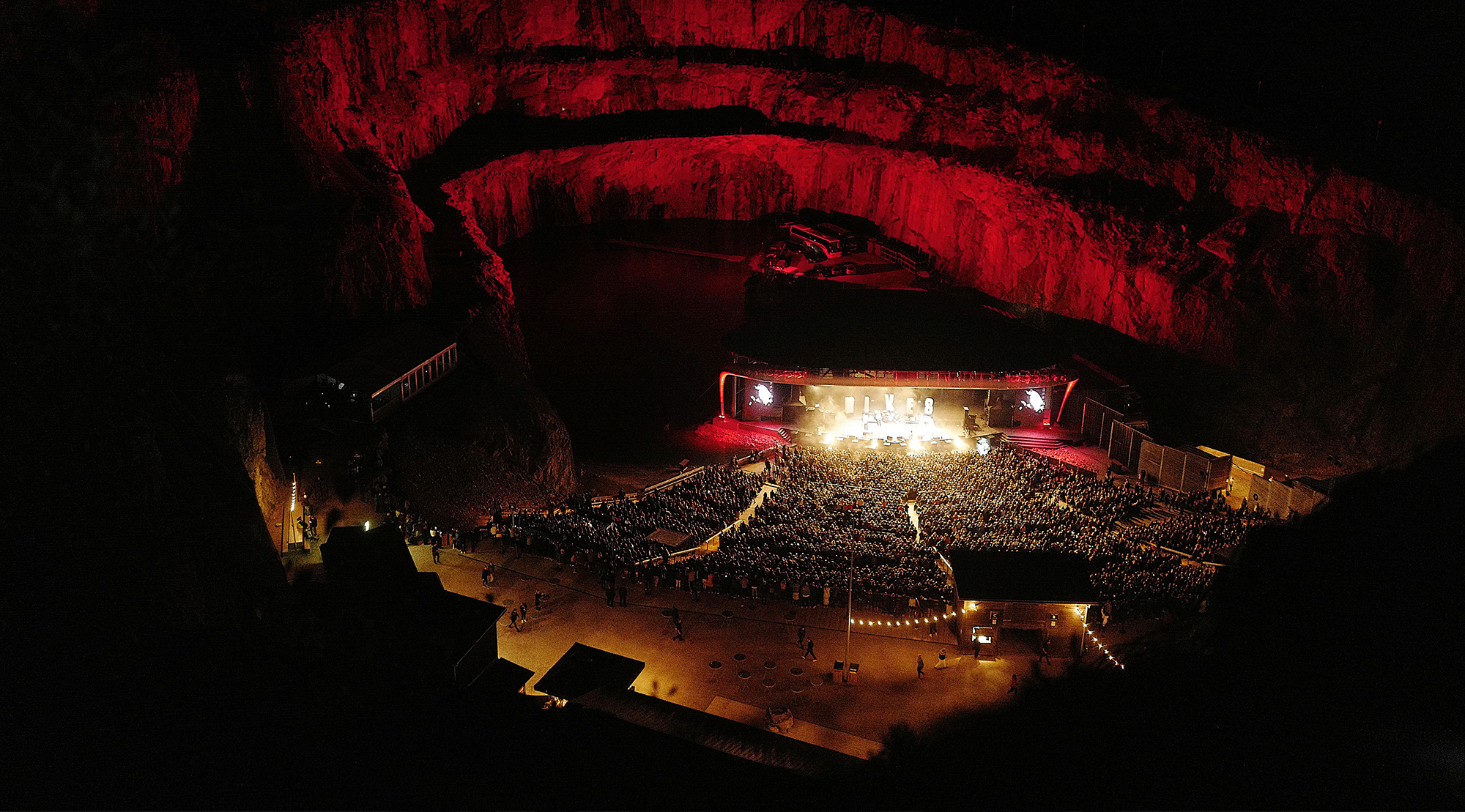 Dalhallas konsertscen i kalkstensbrottet, upplyst från scenen med stor publik framför.