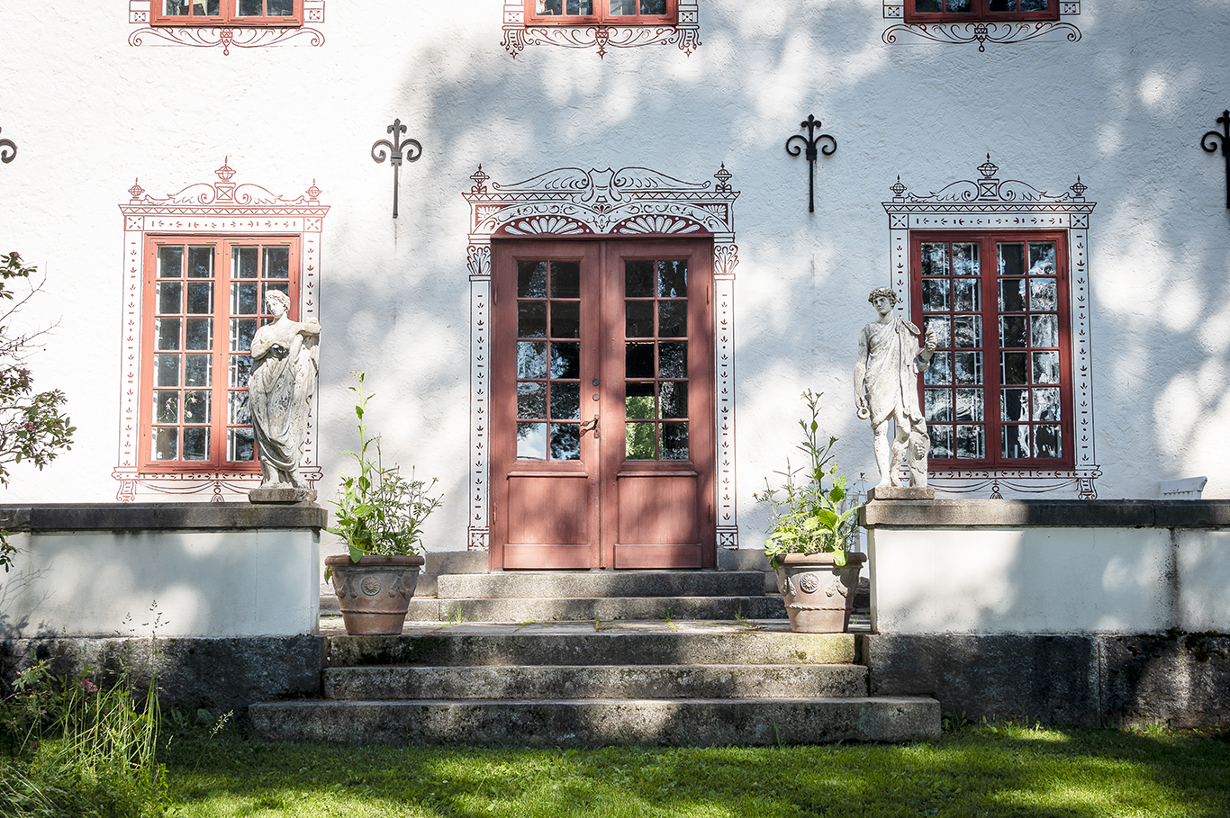 Röda pardörrar och en stentrappa till ett vitt hus med röda fönster.