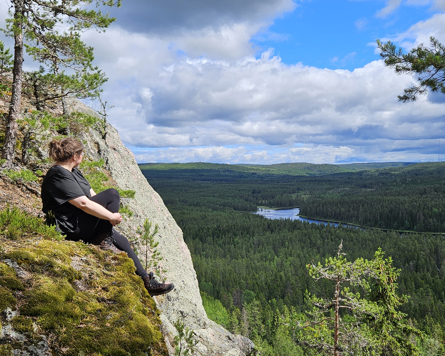 En kvinna sitter på ett berg och ser ut över utsikten sommartid.