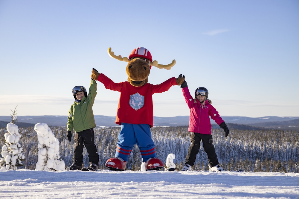 Älgmaskoten Filurius med två barn med uppsträckta händer.