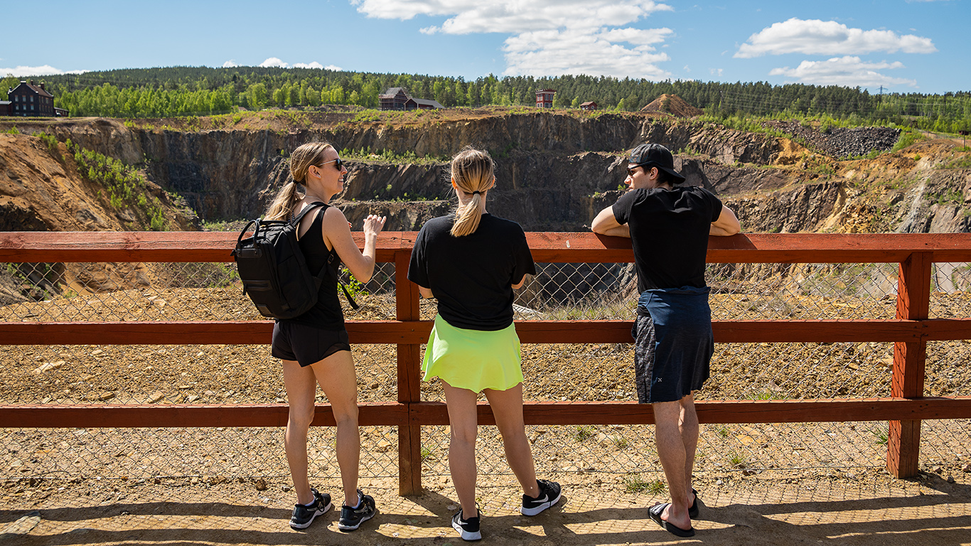 Tre personer lutar sig mot staketet ovanför dagbrottet Stora Stöten vid Falu Gruva.