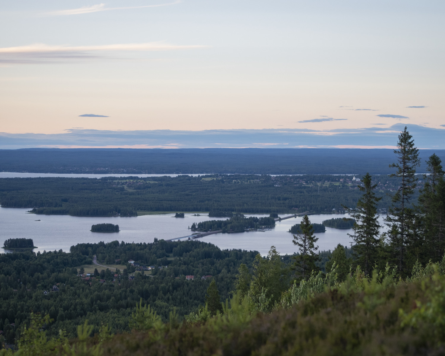 Utsikt från ett berg över skog, sjö och blånande berg.