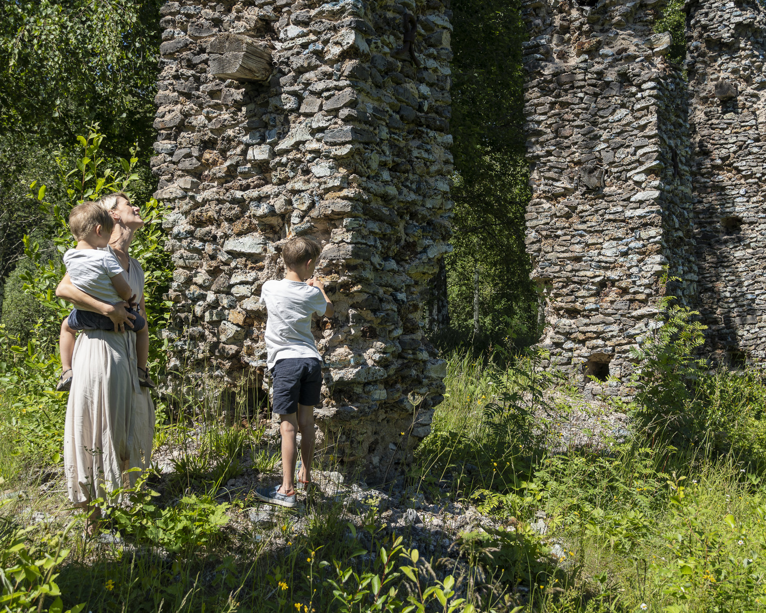 En kvinna och två barn står vid en ruin sommartid.