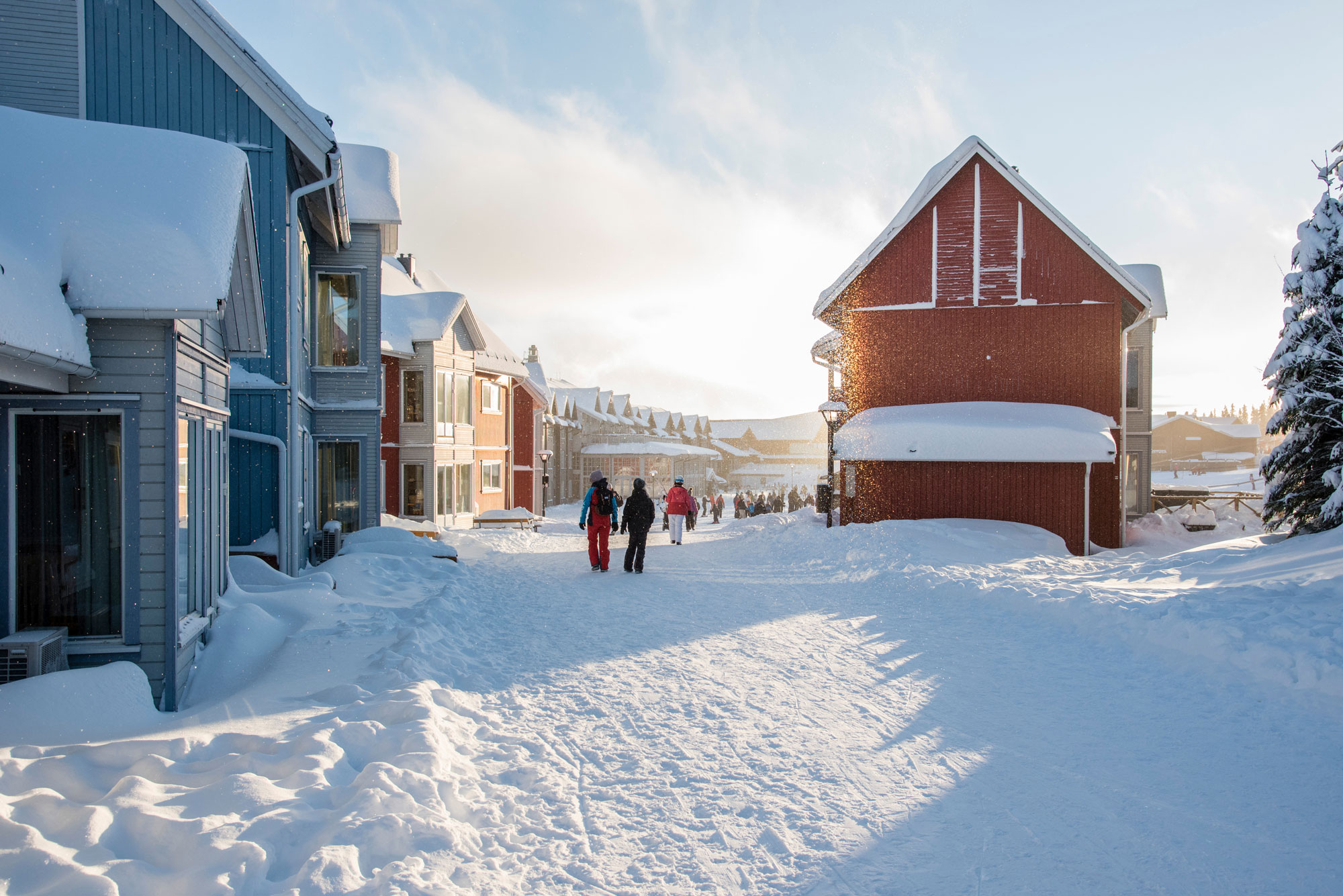 Människor i pjäxor går genom stugby i fjällen.