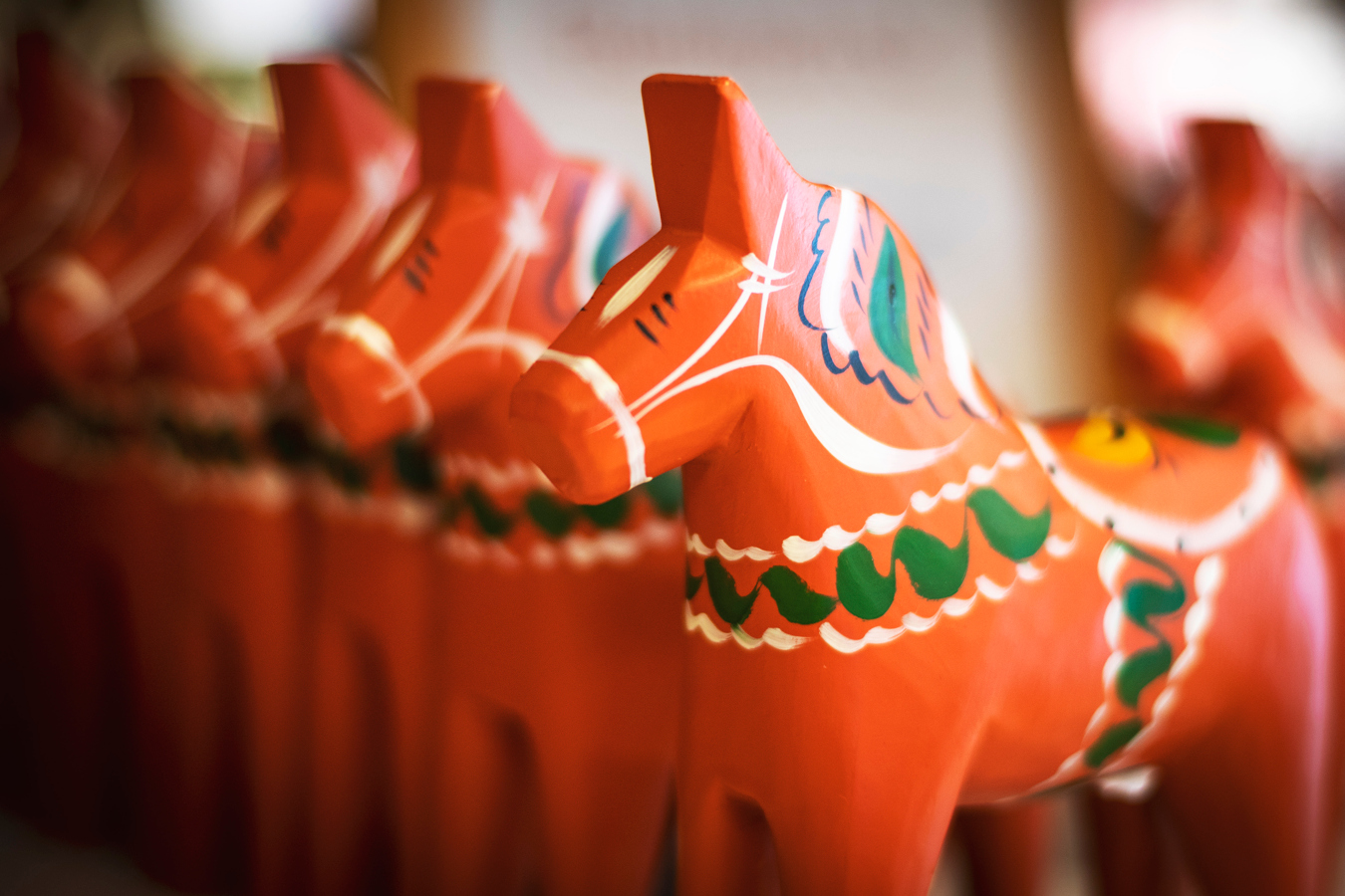 Röda dalahästar med grön kurbitsmålning står på rad.