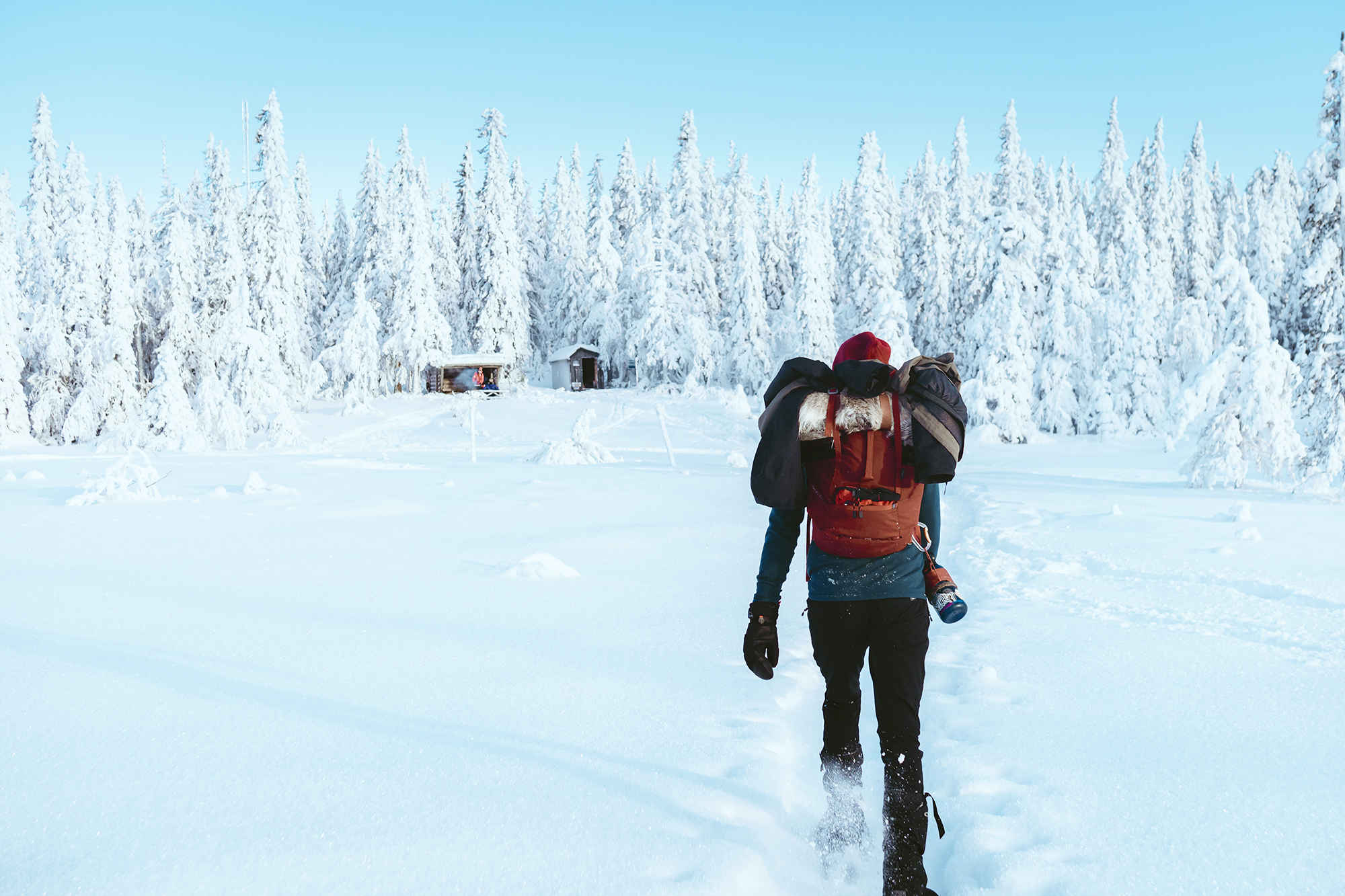 En person med ryggsäck går mot en stuga i snötäckt skog.