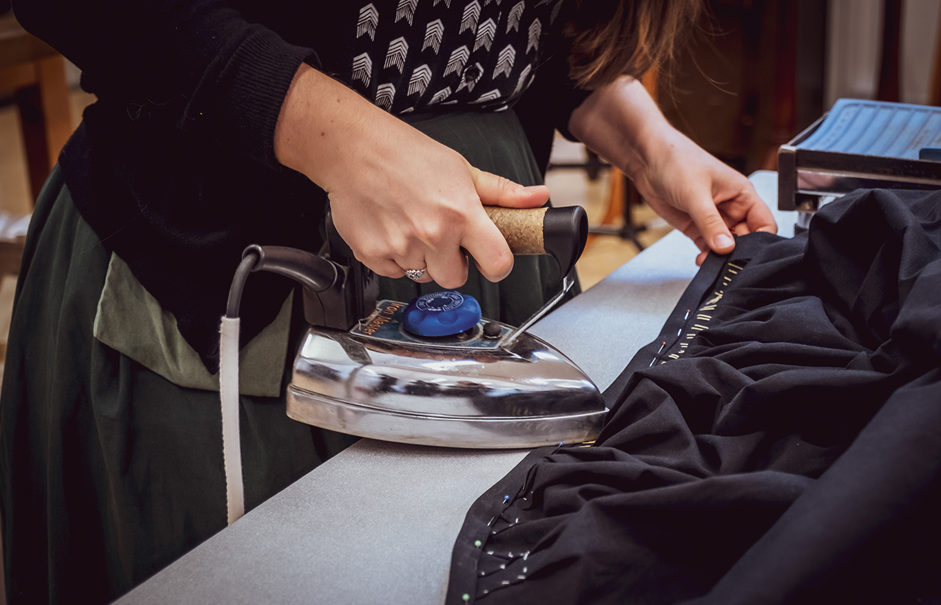 En kvinna stryker en nålad fåll i ett svart tygstycke.