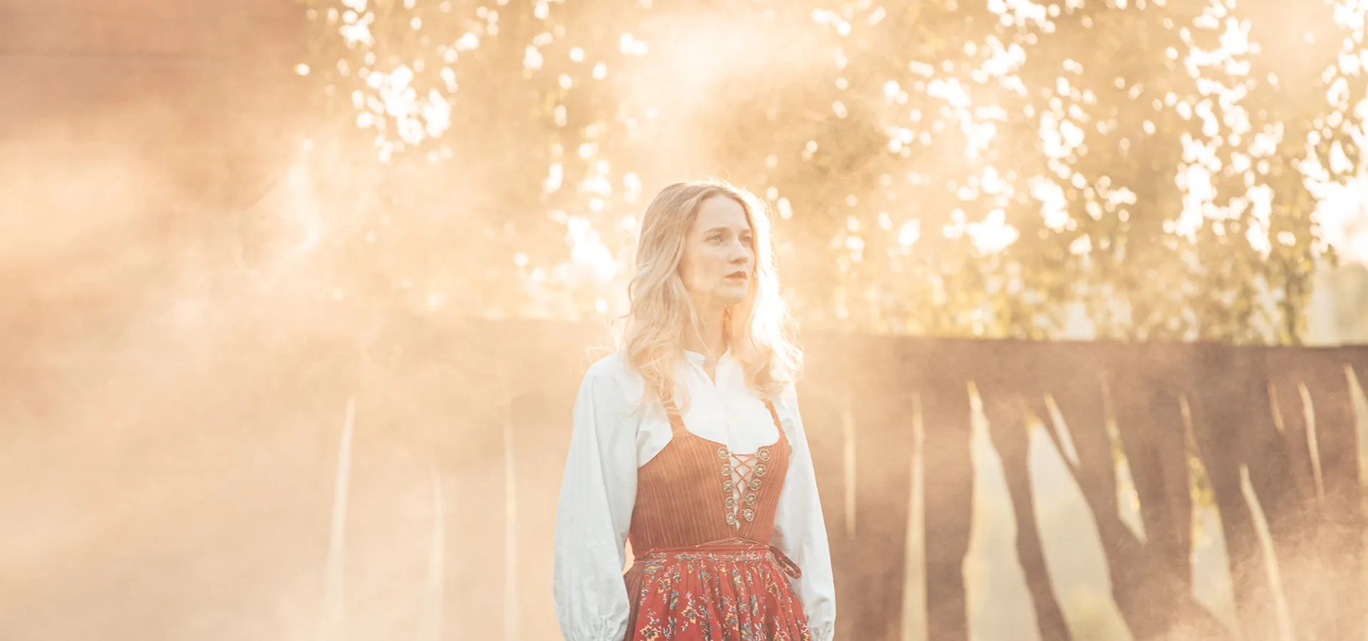 En blond kvinna i folkdräkt står på en scen i motljus.