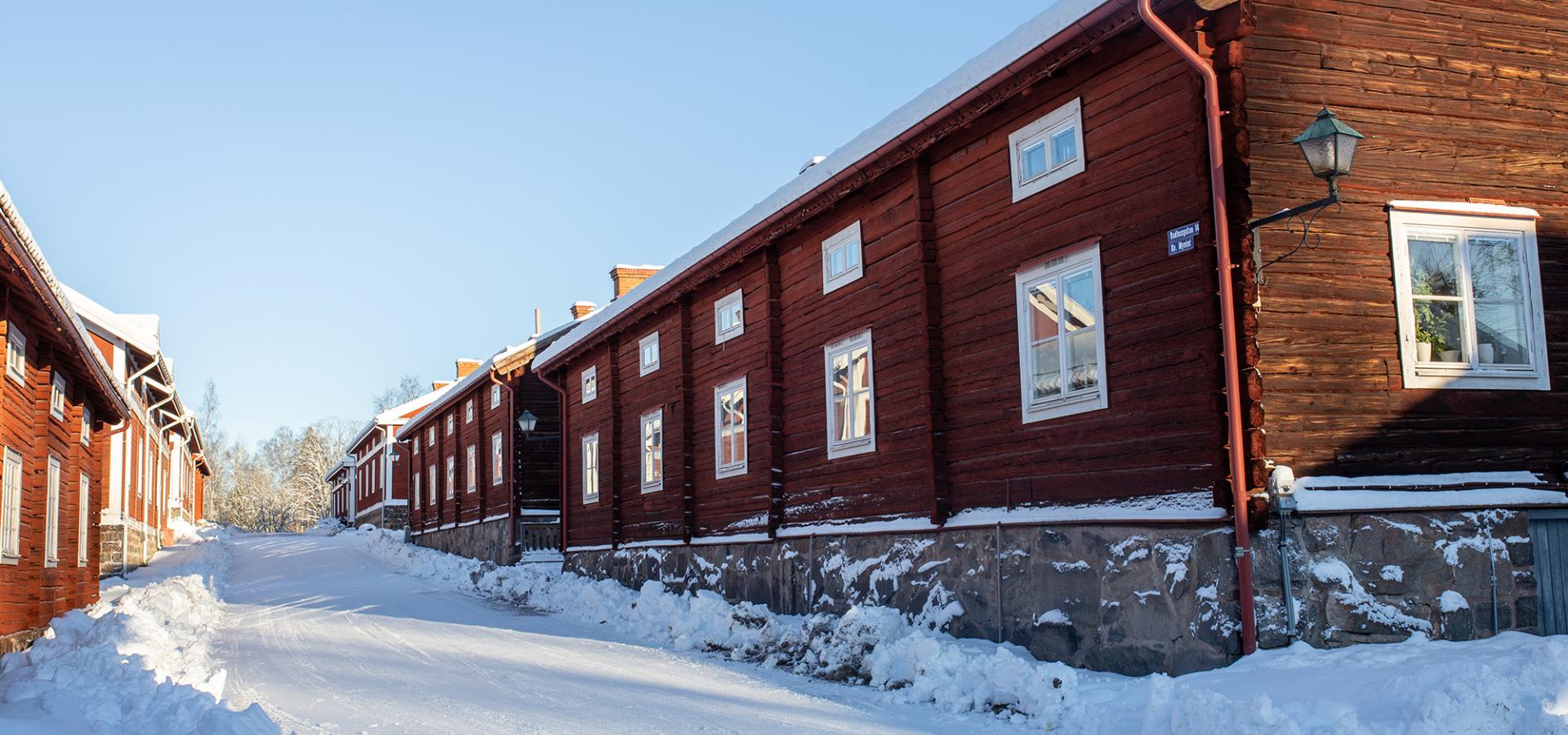 Vintrig gata i Gamla Byn Avesta, röda hus på stengrund med snö på taken.