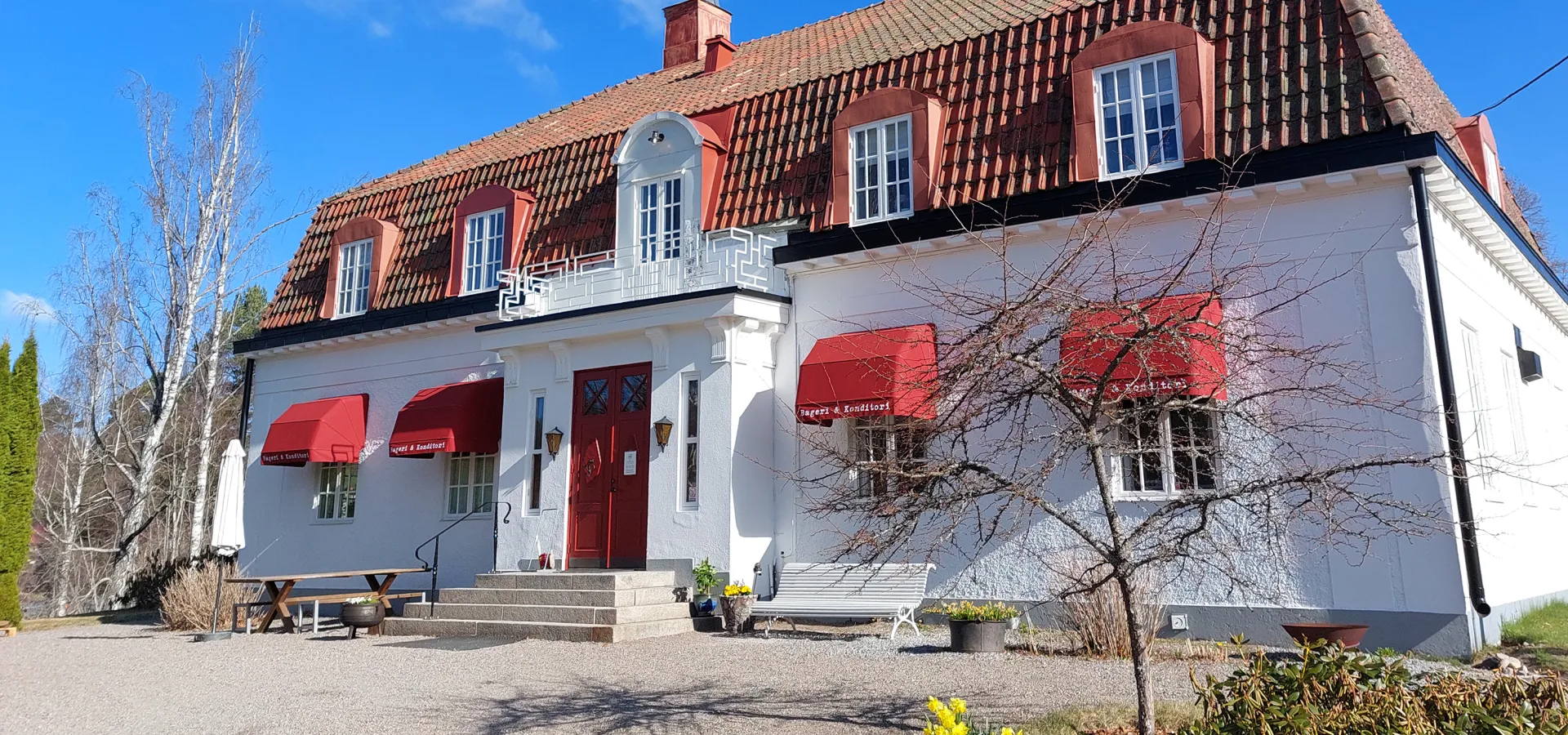 En vit byggnad med tegeltak och röda markiser.