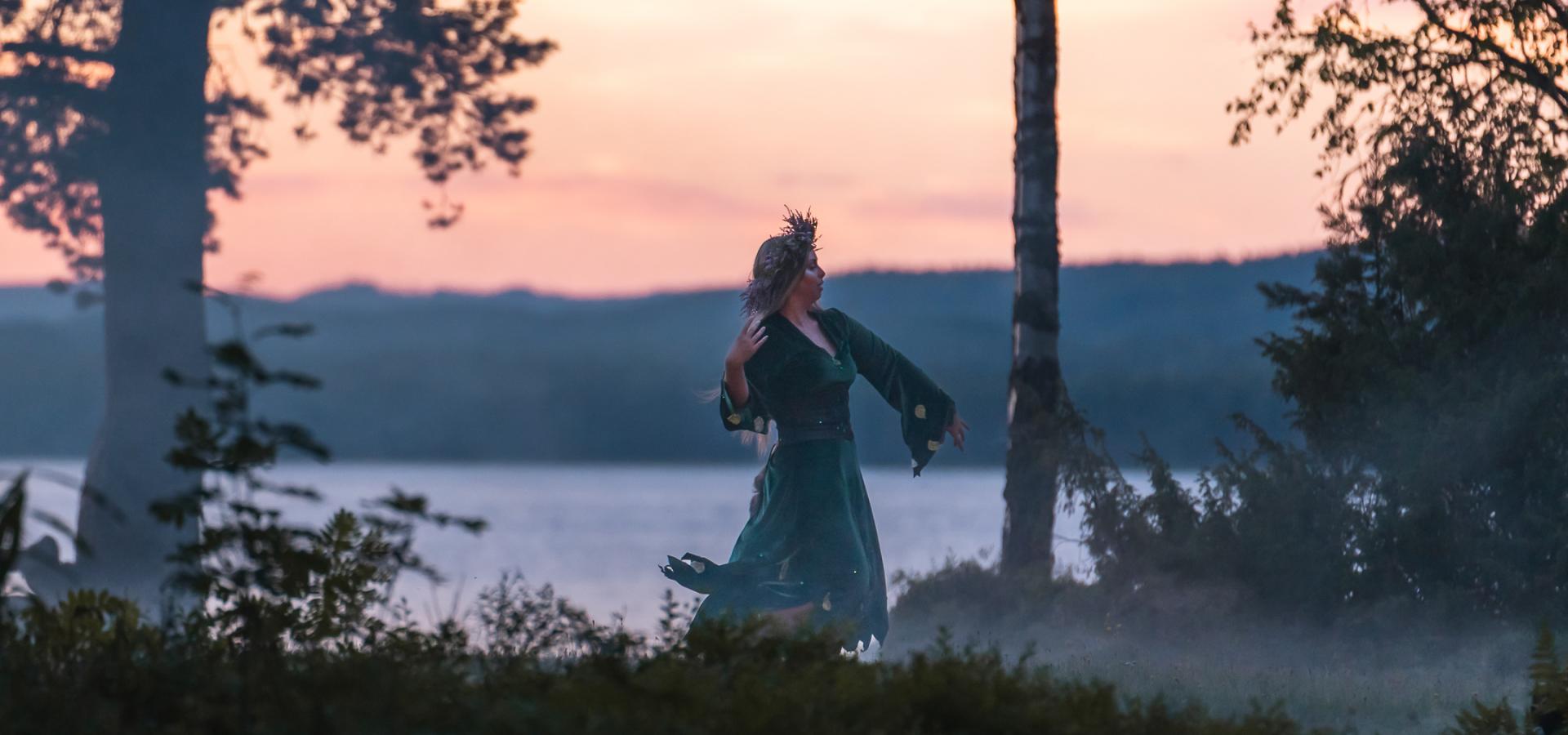 En kvinna dansar i skymning med en sjö i bakgrunden.