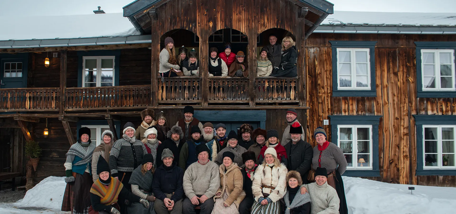 Stor grupp människor i äldre kläder framför ett äldre hus.