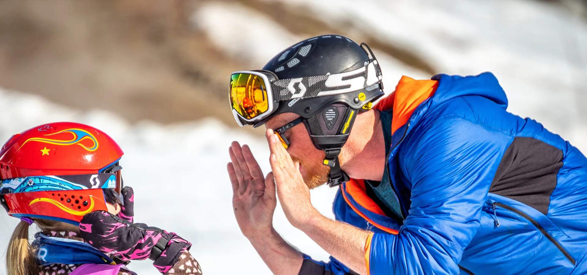 Ett barn och en vuxen med skidhjälmar lyfter händerna mot varandra.