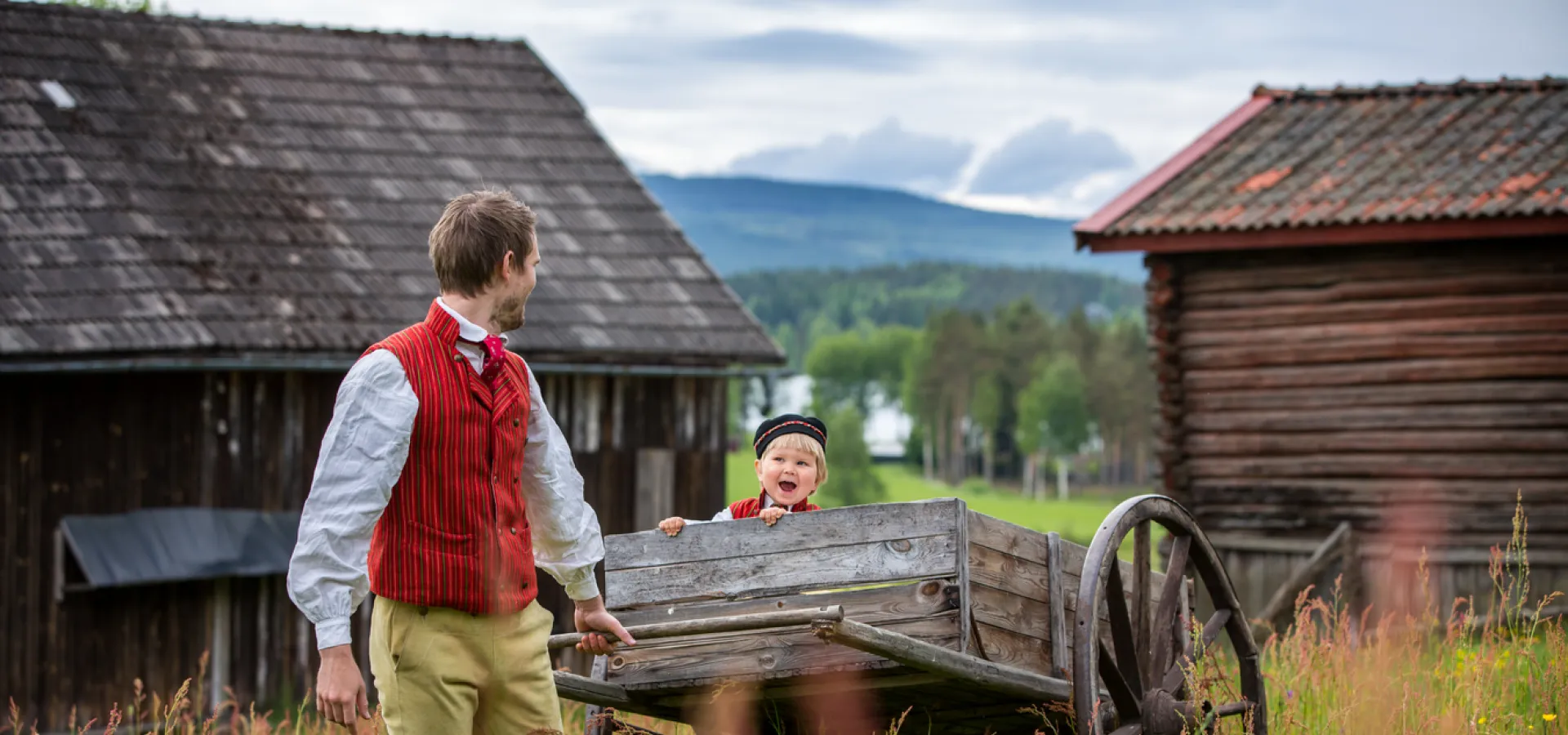 Pappa och son i folkdräkt i fäbodlandskap.
