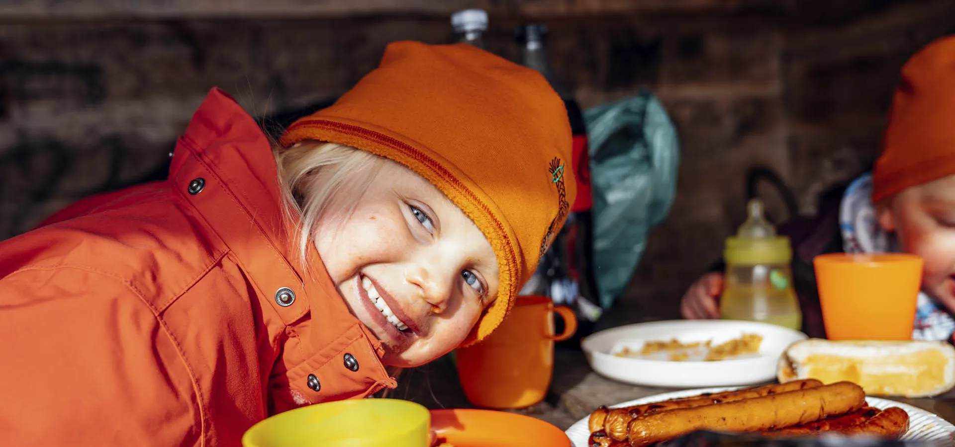 Barn i oranga kläder som äter picknick i ett vindskydd.