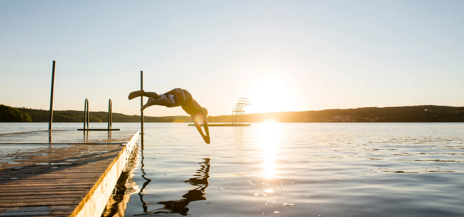 One who dives into the water from the pier at sunset.