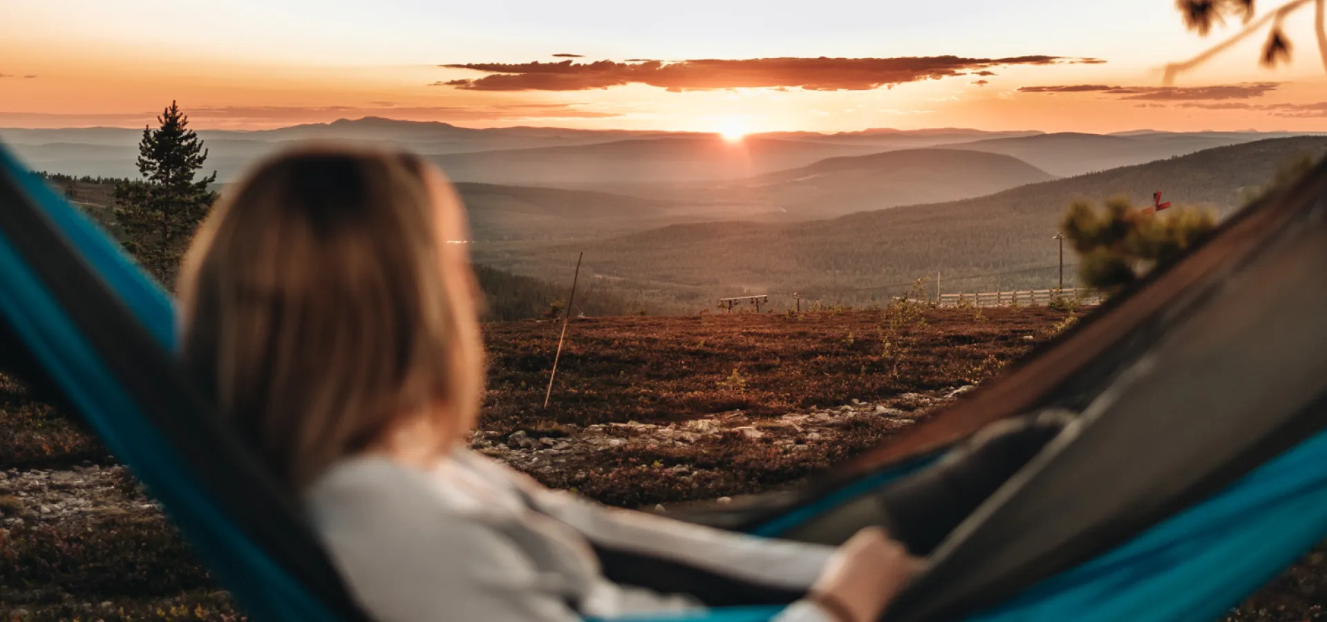 A woman in a hammock looking at the sun set.