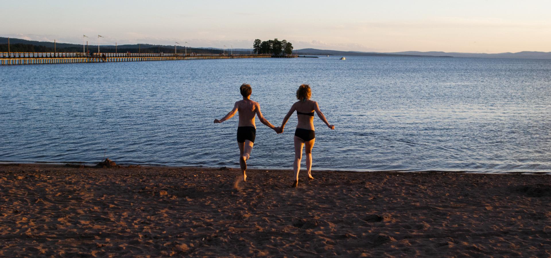 Två barn springer ut i vattnet på stranden.
