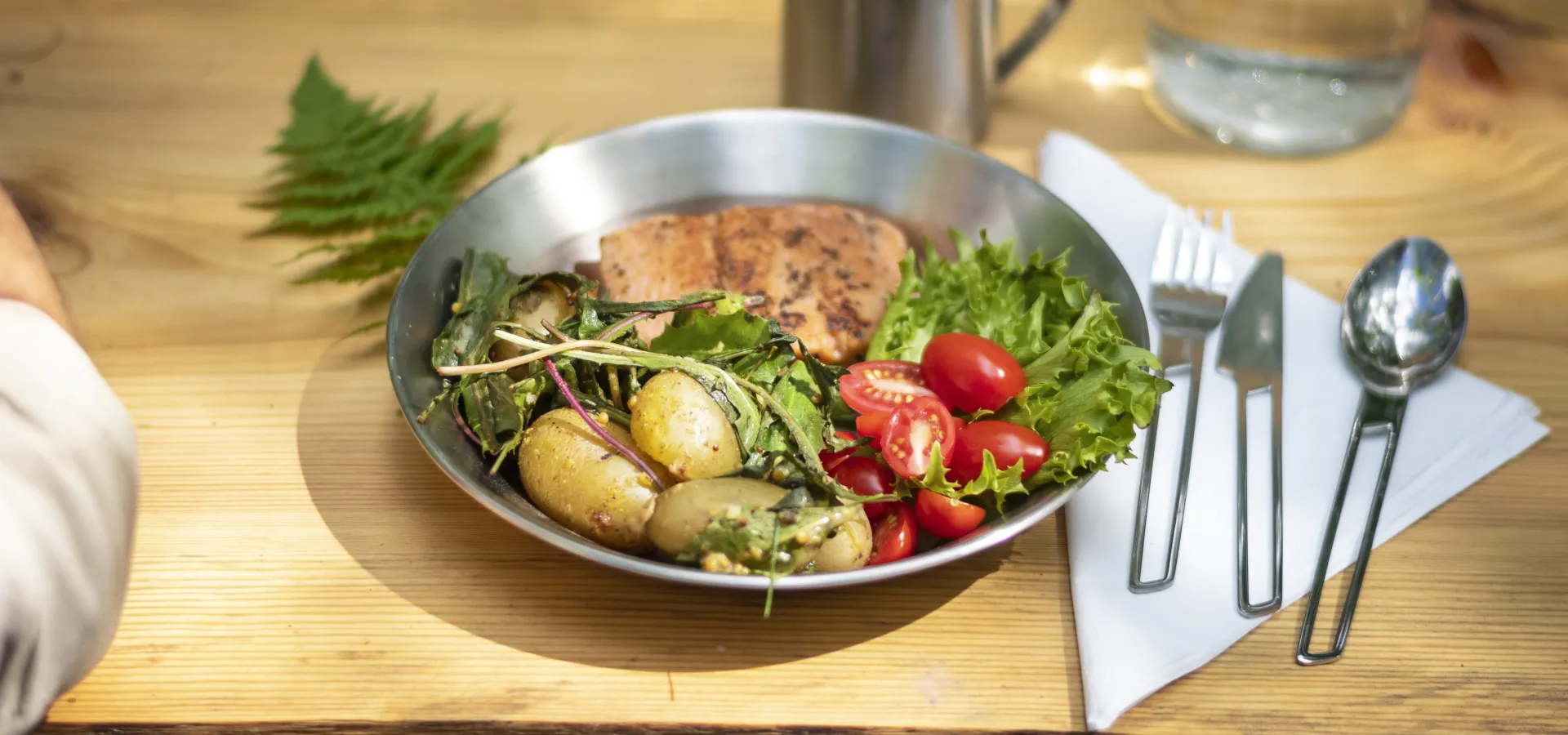 Lax, potatis och sallad vackert upplagt på en plåttallrik utomhus.