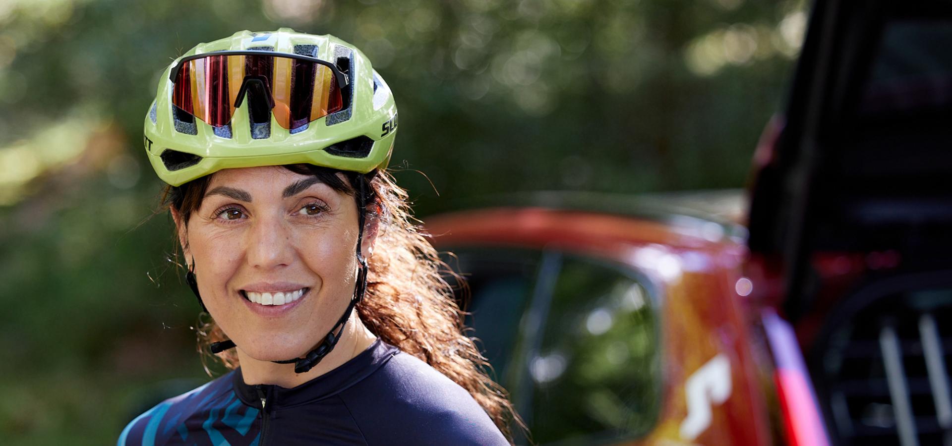 En leende kvinna med långt mörkt hår och grön cykelhjälm.