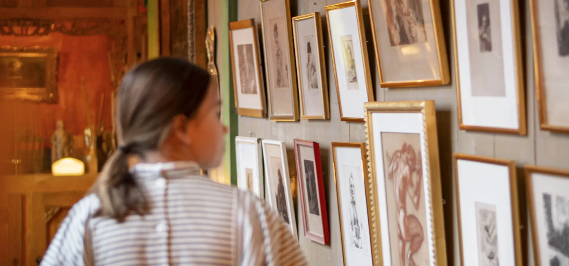 A guide at Carl Larsson-gården walking pass a wall full of paintings.