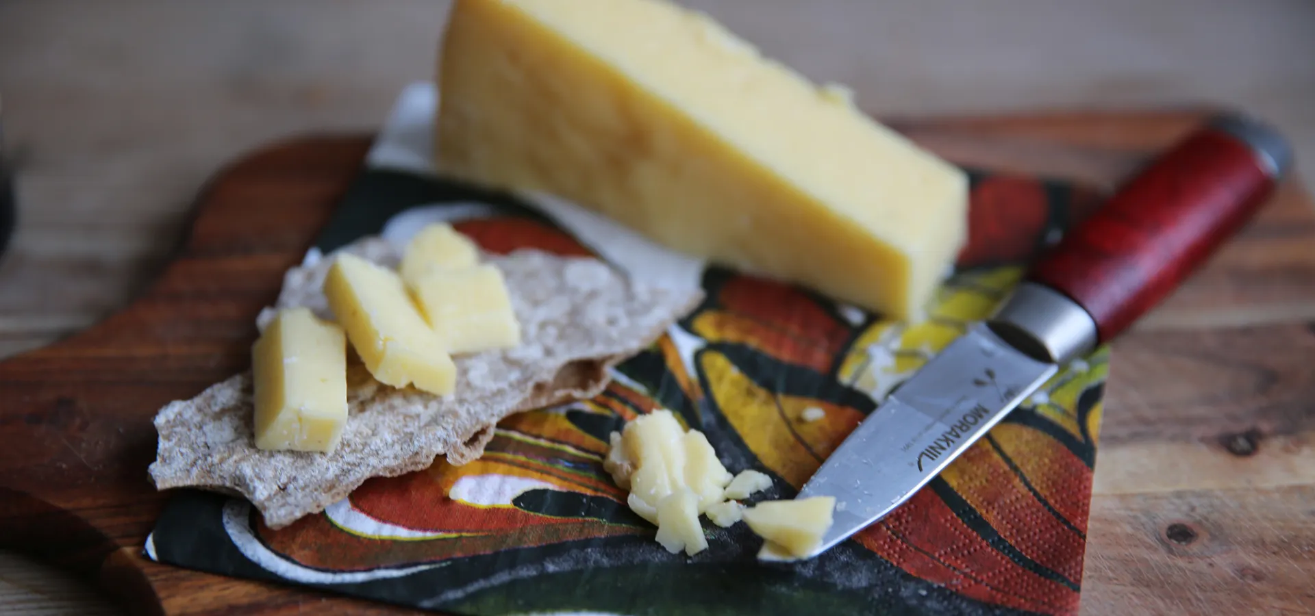 Hårdost skuren i bitar på en träbricka med en fin servett och en kniv bredvid.