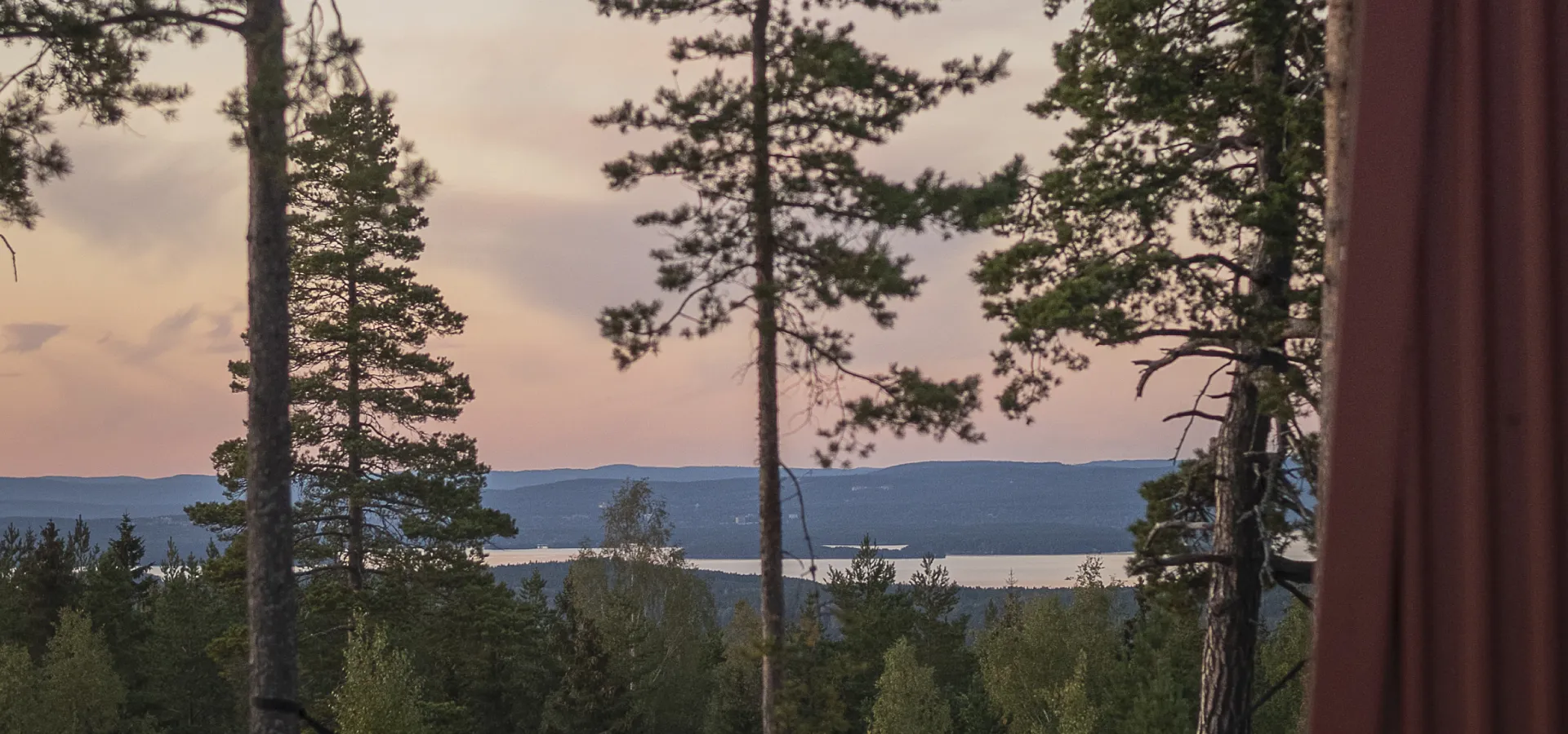Utsikt över skog, sjö och blånande berg i solnedgången sommartid.