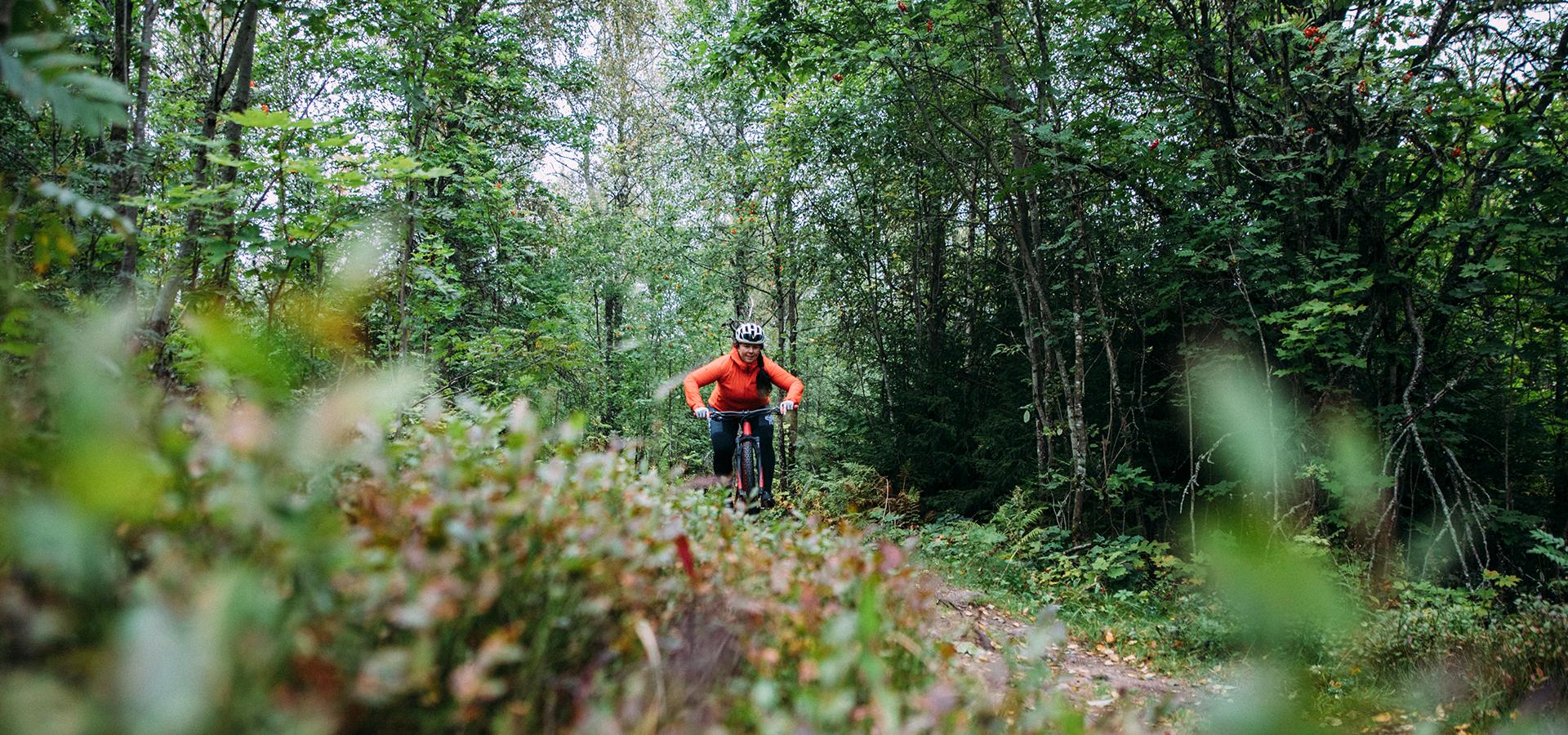 En kvinna i orange jacka cyklar i skogen.