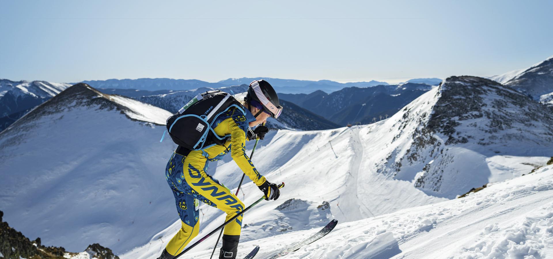 Tove Alexandersson i gul skiddräkt på väg uppför ett fjäll på skidor.