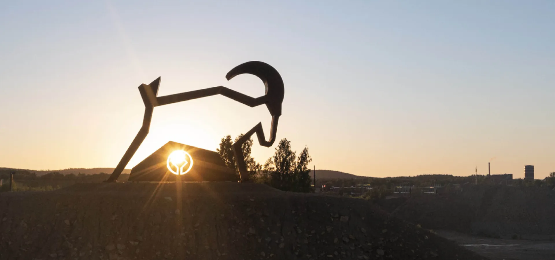 Kopparstaty av Bocken Kåre vid Falu Gruva med solnedgång i bakgrunden.