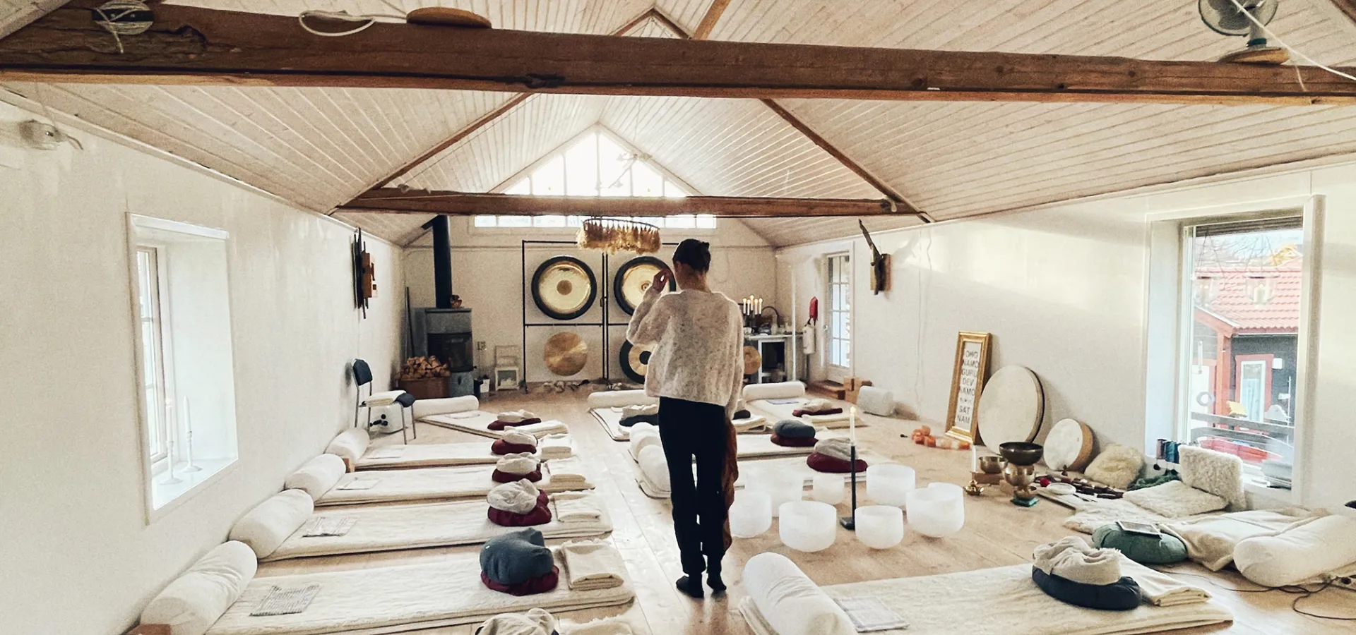 En kvinna går i en yogasal med högt i tak och mattor på golvet.