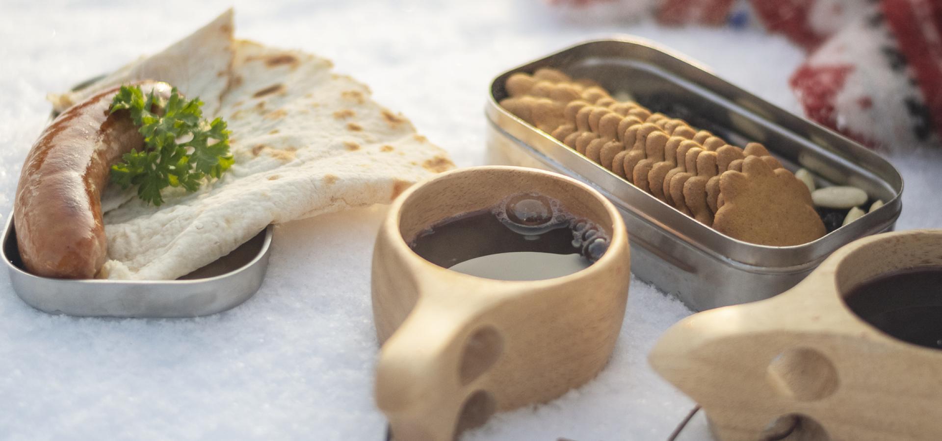 Uppdukad vinterpicknick med kaffe, pepparkakor, grillad korv och tunnbröd.