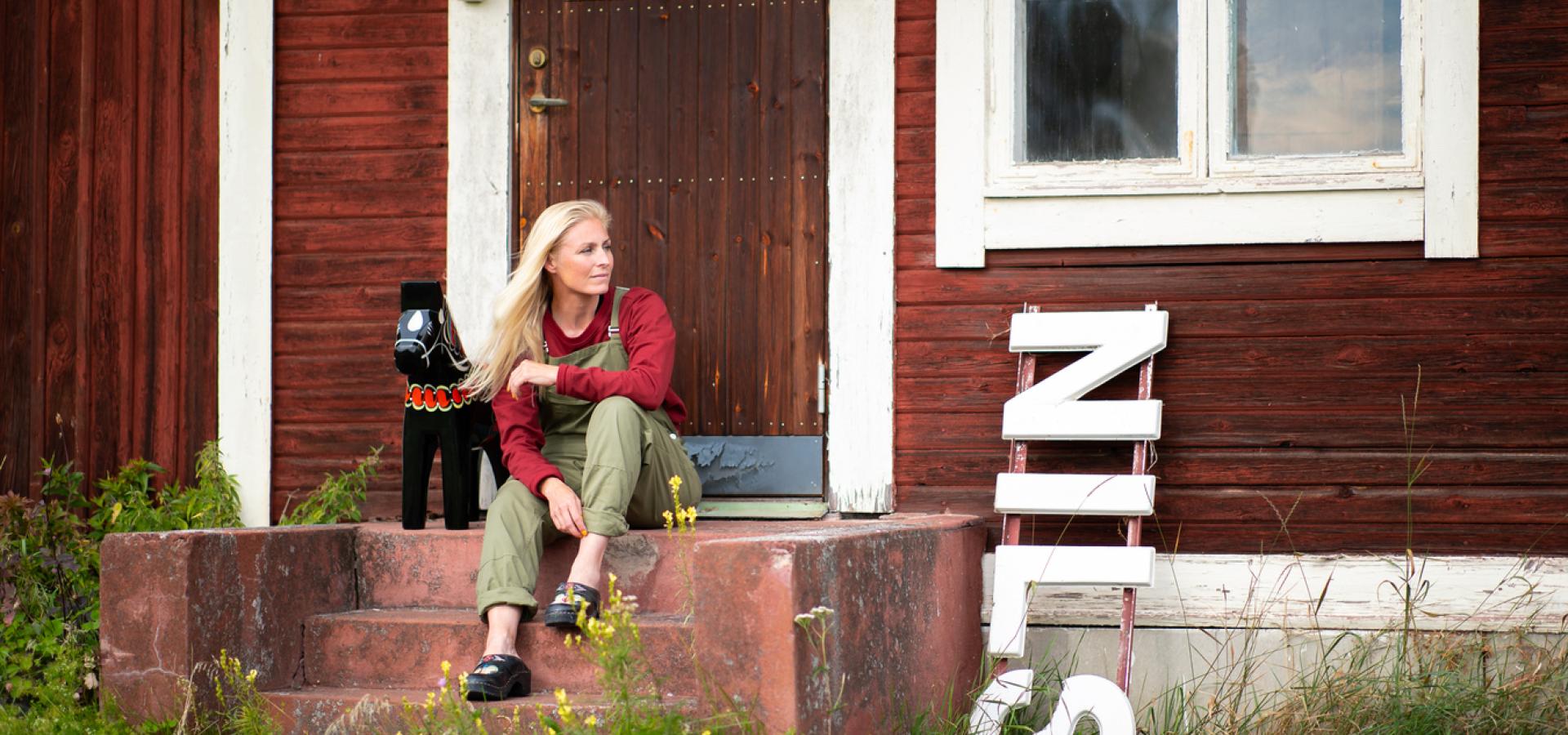 Kvinna sitter på trappa vid dalahästtillverkningen Nils Olsson Dalahästar i Nusnäs.