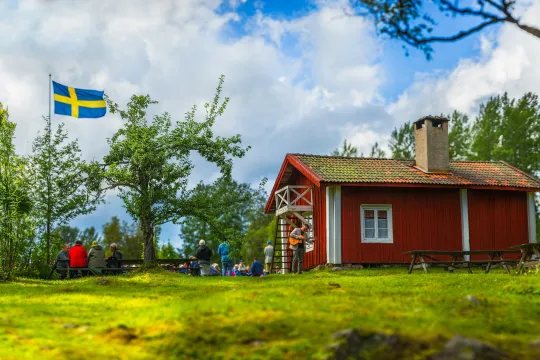 Rödmålad stuga med en flaggstång på gården.