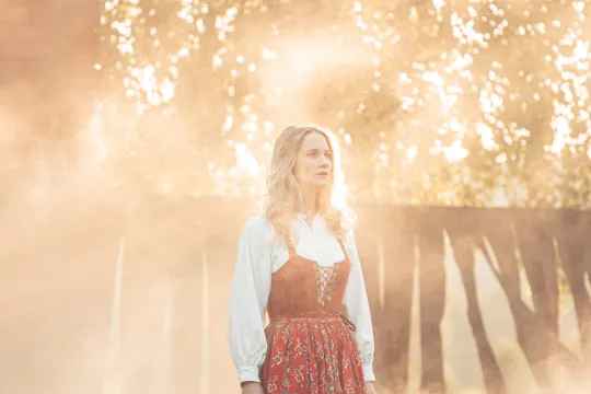 En blond kvinna i folkdräkt står på en scen i motljus.