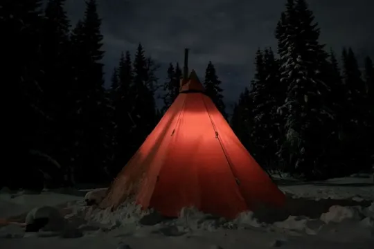 A teepee tent in the middle of the snow out in the forest.