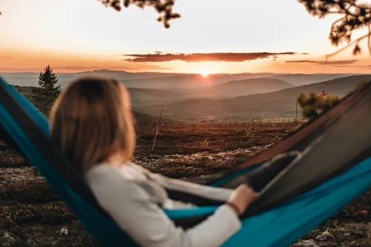 A woman in a hammock looking at the sun set.