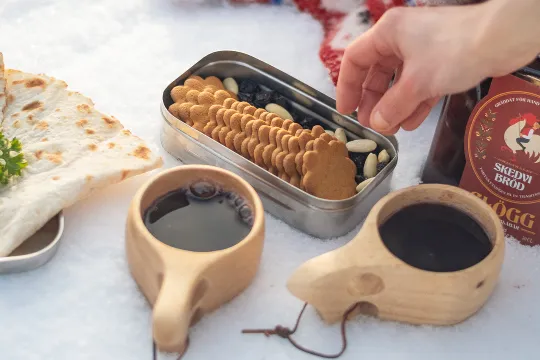 Pepparkakor och glögg i kåsor i snön, en hand tar en kaka.